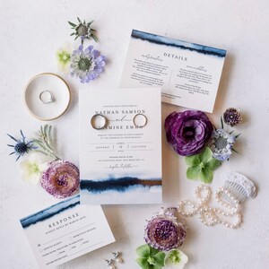 May include: Wedding invitation suite with blue watercolor accents. The invitation features the names "Nathan Samson and Jasmine Emma" with the date "April 17" and the time "5 o'clock". The invitation is surrounded by flowers and a pearl necklace.