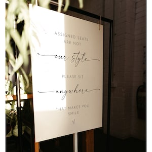 May include: White sign with black text that reads "Assigned seats are not our style. Please sit anywhere that makes you smile."