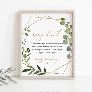 May include: A printable sign with a gold geometric frame and green foliage. The text reads "ring hunt" and "There are rings hidden throughout the shower. Person who finds the most rings by the time the first gift is opened wins a prize! happy hunting".