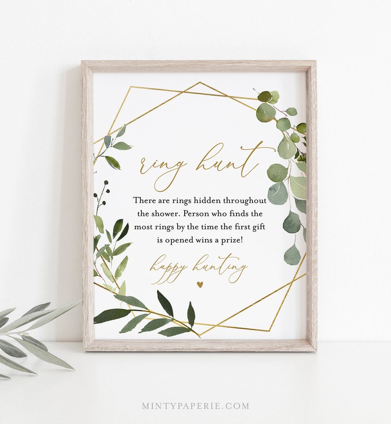 May include: A printable sign with a gold geometric frame and green foliage. The text reads "ring hunt" and "There are rings hidden throughout the shower. Person who finds the most rings by the time the first gift is opened wins a prize! happy hunting".