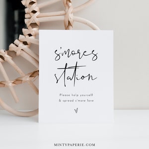 Puede incluir: Un cartel blanco con texto negro que dice "s'mores station" y "Please help yourself & spread s'more love". Hay un pequeño símbolo de corazón en la parte inferior del cartel.
