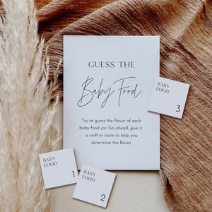 May include: A white card with the text "Guess the Baby Food" and instructions to guess the flavor of each baby food jar. Three white cards with the text "Baby Food" and numbers 1, 2, and 3.