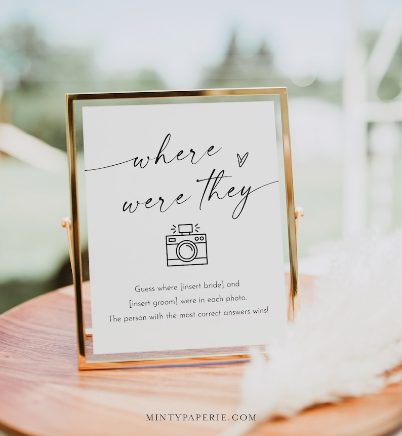 Puede incluir: Un cartel blanco en un marco dorado con el texto "where were they" y un icono de c&aacute;mara. El cartel tambi&eacute;n incluye el texto "Adivina d&oacute;nde [inserta la novia] y [inserta el novio] estaban en cada foto. &iexcl;La persona con la mayor cantidad de respuestas correctas gana!"