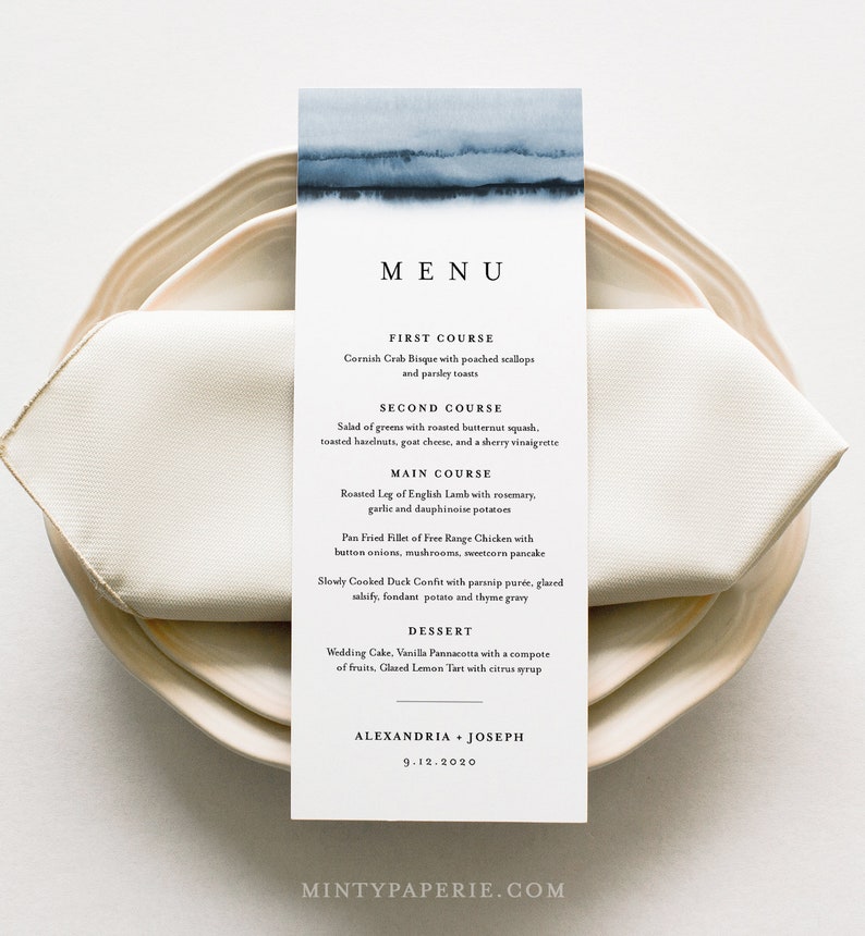 May include: A wedding menu card with a watercolor background in shades of blue. The menu lists the courses: Cornish Crab Bisque, Salad of Greens, Roasted Leg of English Lamb, Pan Fried Fillet of Free Range Chicken, Slowly Cooked Duck Confit, Wedding Cake, Vanilla Pannacotta, and Glazed Lemon Tart. The card also includes the names Alexandria and Joseph and the date 9.12.2020.