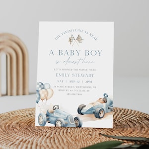 May include: A baby shower invitation with a blue and white checkered race car theme. The invitation says "The finish line is near. A baby boy is almost here." It includes the name Emily Stewart, the date and time of the shower, and the address.