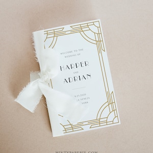 Op de afbeelding: Een wit huwelijks programma met een gouden art deco rand. De tekst luidt "Welkom op de bruiloft van Harper en Adrian 9.23.2020  La Veneza York" en "MintyPaperie.com".