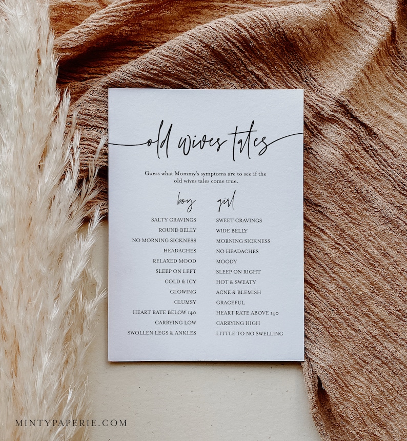 May include: A white card with black text listing old wives' tales about pregnancy symptoms for a baby boy or girl. The card includes symptoms like salty cravings, round belly, no morning sickness, headaches, relaxed mood, sleep on left, cold and icy, glowing, clumsy, heart rate below 140, carrying low, swollen legs and ankles, sweet cravings, wide belly, morning sickness, no headaches, moody, sleep on right, hot and sweaty, acne and blemish, graceful, heart rate above 140, carrying high, little to no swelling.