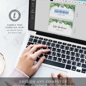 May include: A laptop computer screen displaying a template for a table card with the text "Leslie Henderson, Table One". The template has a tropical leaf design. A hand is typing on the keyboard.
