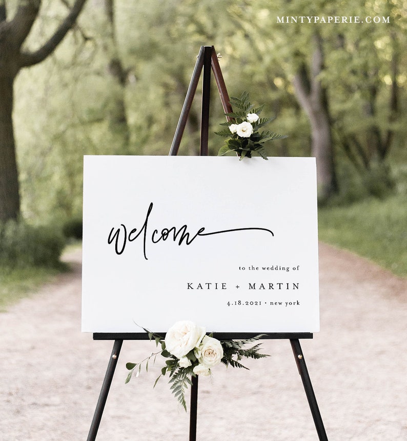 May include: White welcome sign with black calligraphy text on an easel. The sign reads "Welcome" to the wedding of Katie + Martin 4.18.2021 - New York.
