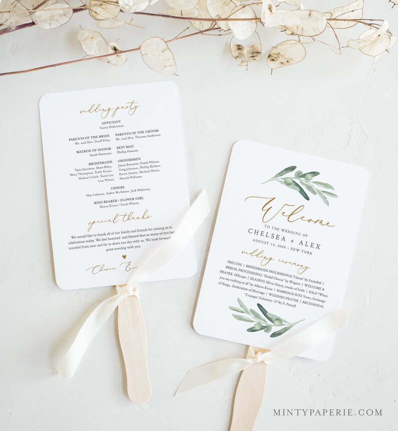 May include: A white wedding program fan with a green olive branch design and gold lettering. The text reads "Welcome to the wedding of Chelsea + Alex August 14, 2020 New York".