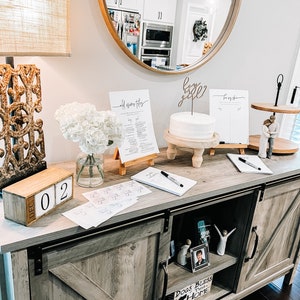 May include: A wooden table with a rustic finish, decorated for a baby shower. There is a cake with a "baby girl" topper, a sign that says "old wives tales", and a sign that says "boy or girl". There is also a wooden block calendar that says "Dec 02".