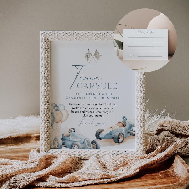 May include: White frame with a blue and white time capsule sign. The sign says "Time Capsule" and "To be opened when Charlotte turns 18 in 20XXI". There are blue and white race cars and balloons on the sign. There is a white card with lines for writing on it.