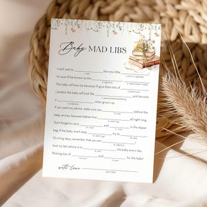 May include: A printable baby shower game card with the title "Baby Mad Libs". The card has a floral design and a stack of books. The game instructions are written in a playful, lighthearted tone.