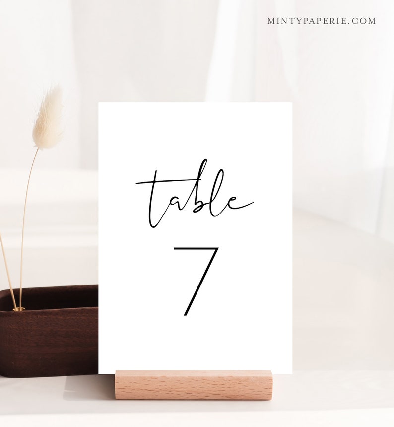 Puede incluir: Tarjeta de n&uacute;mero de mesa blanca con caligraf&iacute;a negra que dice "mesa 7".