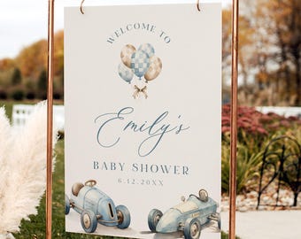 以下が含まれることがあります： 青と茶色の風船、青いビンテージカー、そして「Emily's Baby Shower 6.12.20XXへようこそ」という文字が書かれた白いウェルカムサイン。