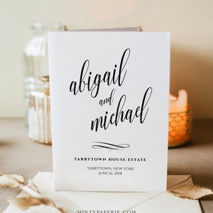 以下が含まれることがあります： 白い結婚式の招待状に、黒い書体で「abigail and michael」と書いてあり、その下に「Tarrytown House Estate, Tarrytown, New York, June 16, 2018」と書いてあります。