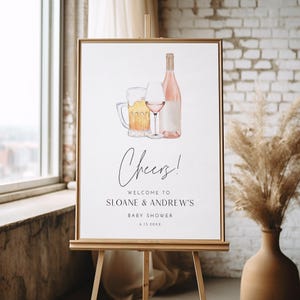 May include: A framed sign on an easel with illustrations of beer, wine, and a bottle. The sign says "Cheers!" and welcomes guests to Sloane & Andrew's baby shower.