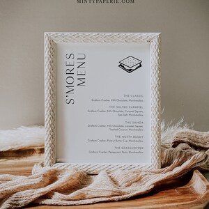 May include: A white framed menu with a black and white illustration of a s'more. The menu lists different s'more variations with ingredients, including The Classic, The Salted Caramel, The Samoa, The Nutty Buddy, and The Grasshopper.
