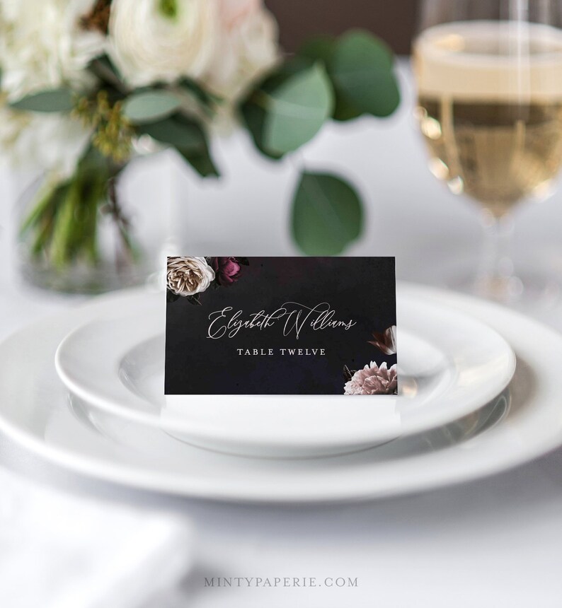 May include: A black place card with a floral design and the text "Elizabeth Williams, Table Twelve".