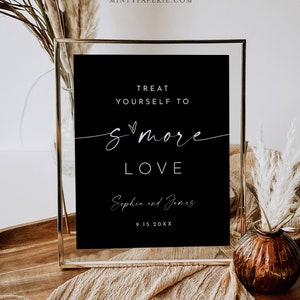 May include: A black sign in a gold frame with white text that reads "Treat Yourself to S'more Love" with the names Sophia and James and the date 9.15.20XX. The sign is on a wooden tray with decorative elements.