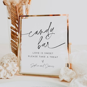 May include: A gold-framed sign with the text "candy bar" in a cursive font. The sign also includes the text "Love is sweet, please take a treat" and "Sophia and James" with a heart symbol.