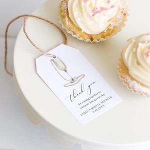 Op de afbeelding: Een wit bedankkaartje met een illustratie van een champagne glas en een parelketting. De tekst luidt: "Bedankt dat je samen bent gekomen om deze speciale dag te vieren. Emily's bruiloft 6.12.20XX"