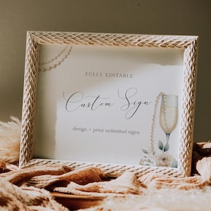 Op de afbeelding: Een wit frame met een decoratief ontwerp omringt een printbaar bord met de tekst "FULLY EDITABLE Custom Sign design + print unlimited signs". Het bord toont een aquarel-illustratie van een champagnefluit met een parelketting eroverheen.