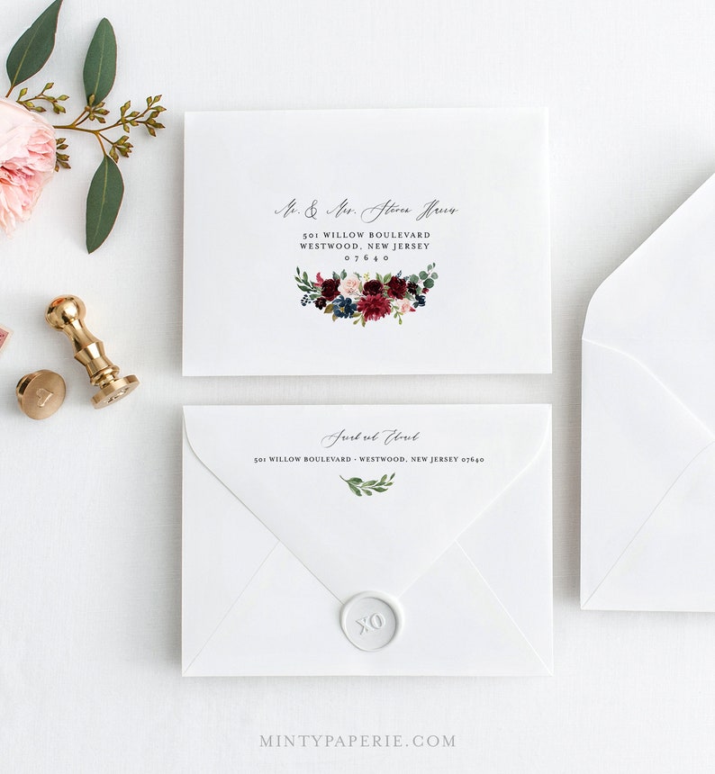 May include: Two white envelopes with calligraphy addressing. The top envelope has a floral design with burgundy, pink, and blue flowers. The bottom envelope has a wax seal with the letters XO.