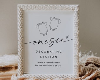 May include: White frame with a sign that says "onesie decorating station" with two baby onesie outlines and the text "Make a special onesie for the new bundle of joy."