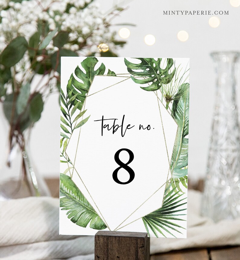 May include: White table number card with a gold geometric frame and green tropical leaves. The card says "Table no. 8".
