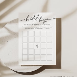 May include: A printable bridal bingo card with a black and white design. The card has 25 squares with a heart in the center square. The text "bridal bingo" is written in cursive at the top of the card. The text "WHAT WILL THE BRIDE-TO-BE RECEIVE?" is written in all caps below the title. The text "Fill in the squares with your best guesses. Mark the squares that match as she opens her gifts. First person to get 5 in a row wins!" is written in all caps below the instructions.