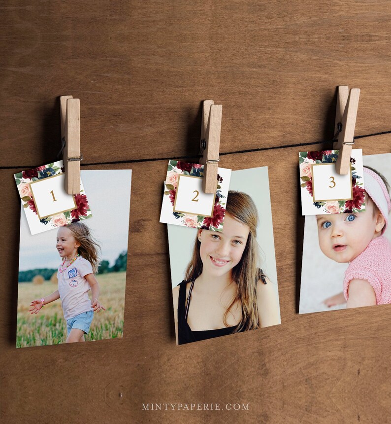 May include: Three photos are displayed on a wooden wall with clothespins. Each photo has a floral design card with a gold number on it. The numbers are 1, 2, and 3. The photos show a young girl running, a teenage girl smiling, and a baby looking at the camera.