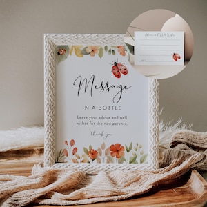 May include: A white framed sign with a floral design and a ladybug. The sign says "Message in a Bottle" and "Leave your advice and well wishes for the new parents. Thank you."
