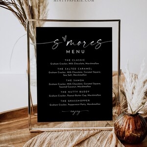 May include: A black framed sign with a white handwritten menu for s'mores. The menu lists different s'mores variations with ingredients like milk chocolate, caramel squares, toasted coconut, peanut butter cups, and peppermint patties.