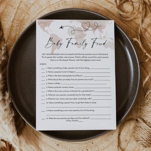 May include: A printable baby shower game called "Baby Family Feud". The game features a light brown background with a world map design and a heart-shaped symbol. The game asks players to guess the top answers to 12 questions about babies and new parents.