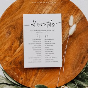 May include: A white card with black text that says "Old Wives Tales" and lists symptoms for a baby boy or girl. The card is on a wooden surface with dried flowers.