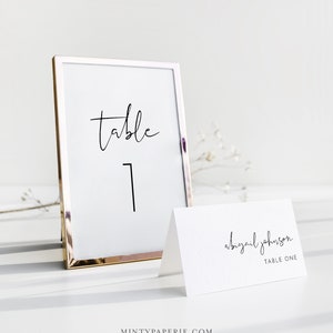 Puede incluir: Una tarjeta de n&uacute;mero de mesa con marco dorado, la palabra "table" y el n&uacute;mero "1" en caligraf&iacute;a negra. Una tarjeta de lugar blanca con el texto "Abigail Johnson Table One" en caligraf&iacute;a negra.