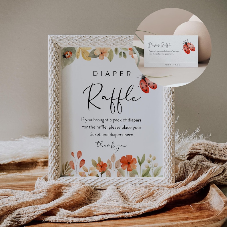May include: A white frame with a floral design and a sign that says "DIAPER Raffle". The sign says "If you brought a pack of diapers for the raffle, please place your ticket and diapers here. Thank you". There is a small card with the text "Diaper Raffle" and a ladybug design.