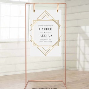 May include: A copper-colored metal wedding sign stand holding a white sign with gold geometric art deco design. The sign reads "WELCOME TO THE WEDDING OF HARPER AND ADRIAN SEPTEMBER 23, 2021 MIDDLETON, NEW YORK."