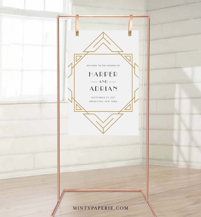 May include: A copper-colored metal wedding sign stand holding a white sign with gold geometric art deco design. The sign reads "WELCOME TO THE WEDDING OF HARPER AND ADRIAN SEPTEMBER 23, 2021 MIDDLETON, NEW YORK."