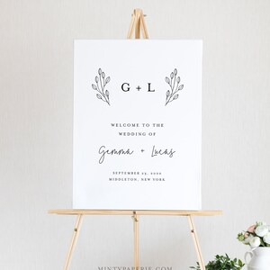May include: A white wedding welcome sign with black text and simple floral illustrations. The sign reads "G + L Welcome to the Wedding of Gemma + Lucas September 23, 2020 Middleton, New York".