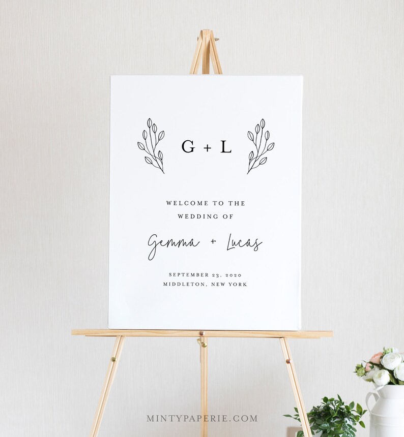 May include: A white wedding welcome sign with black text and simple floral illustrations. The sign reads "G + L Welcome to the Wedding of Gemma + Lucas September 23, 2020 Middleton, New York".
