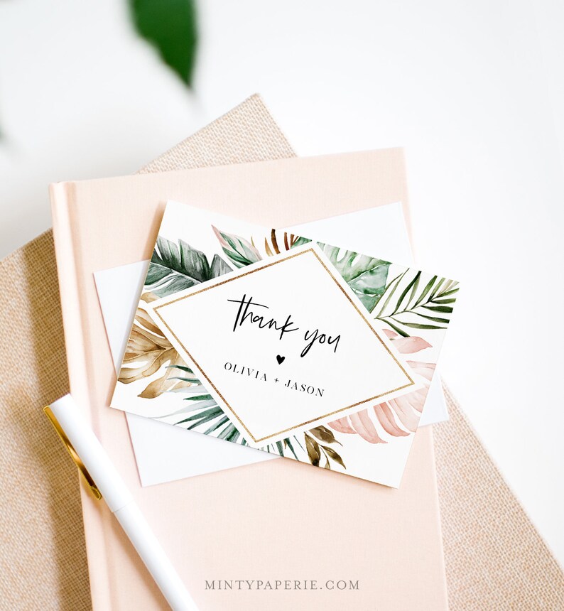 May include: A white thank you card with a gold diamond frame and tropical leaf design. The text "Thank you" is written in black script font. The names "Olivia + Jason" are written below the text.