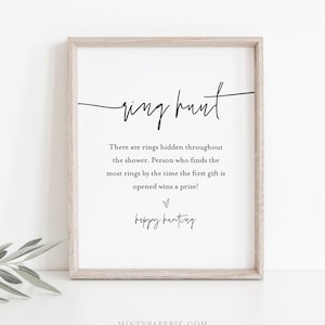 May include: A printable sign with the text "ring hunt" in cursive script. The sign instructs guests to find rings hidden throughout the shower, with the person who finds the most rings by the time the first gift is opened winning a prize. The sign also includes the text "happy hunting" in cursive script.