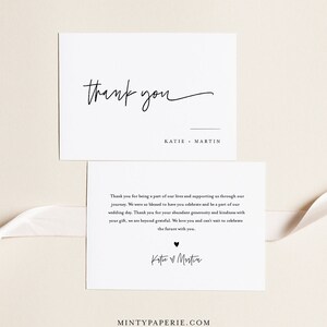 May include: A white thank you card with black text. The card says "Thank you" in cursive and "Katie Martin" in a simple font. The card also includes a smaller card with a thank you message and the couple's names in cursive.