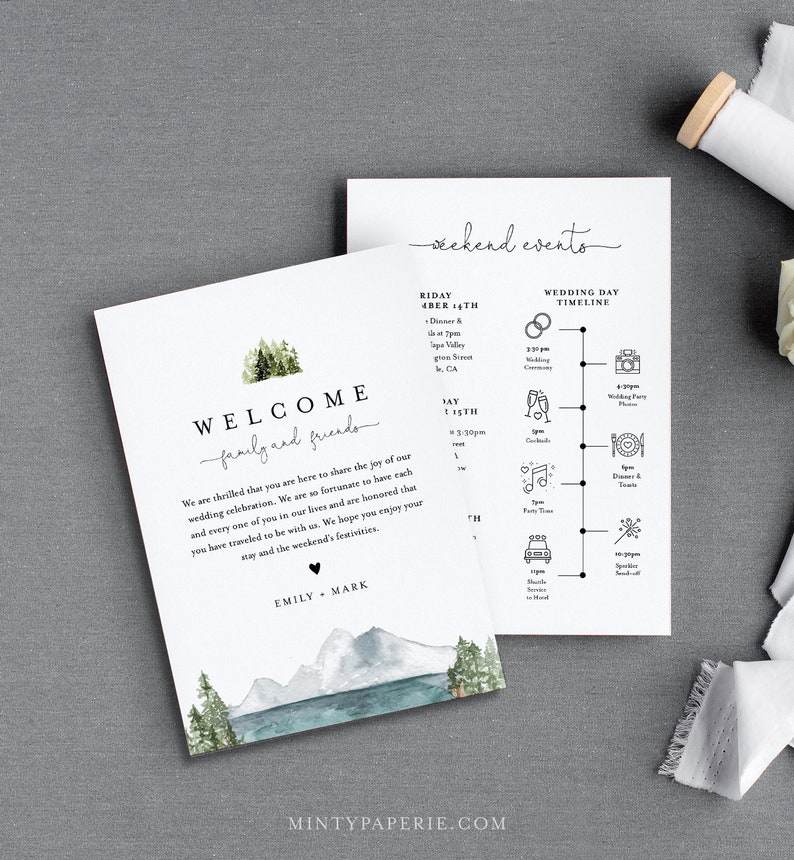May include: A welcome sign with a watercolor illustration of mountains, trees, and a lake. The text reads "Welcome family and friends" and "Emily + Mark". The sign also includes a wedding day timeline with icons for the ceremony, cocktails, party time, dinner and toasts, and sparkler send-off.
