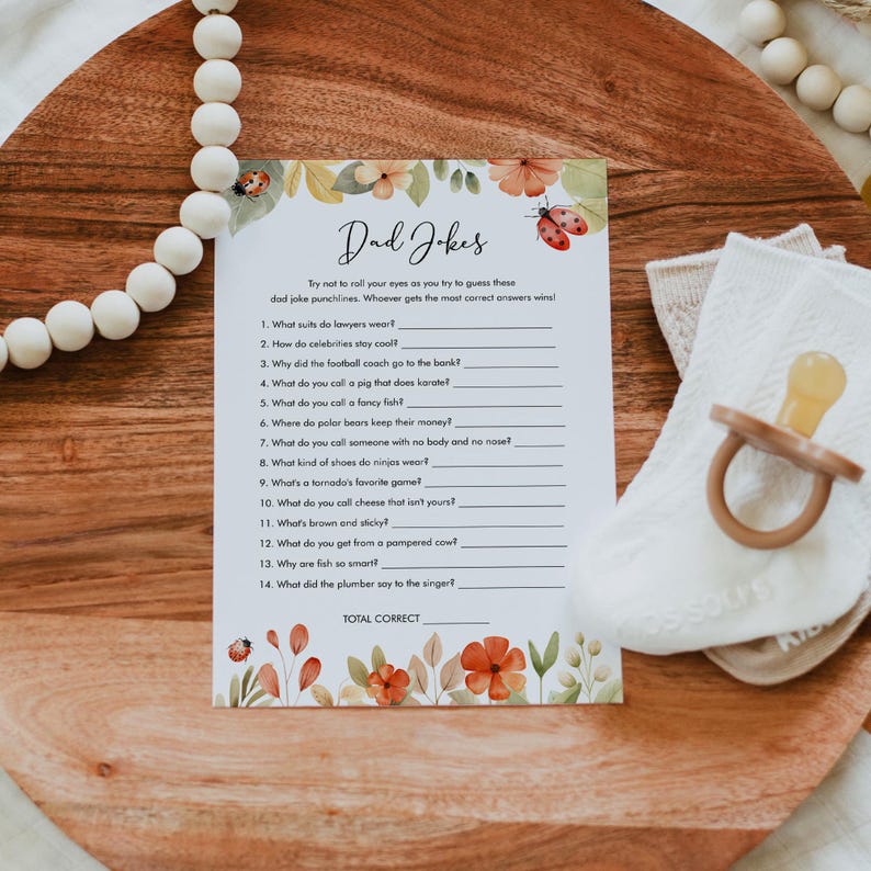 May include: A printable game card with a floral border and a title that reads "Dad Jokes". The card features a list of 14 dad jokes with blank lines for players to write in their answers.
