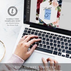 May include: A laptop computer with a screen displaying a floral wedding table number template. The template is a hexagonal shape with a blue background and the text "table 5" in white. The template is surrounded by a floral design with burgundy, pink, and blue flowers.