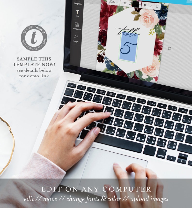 May include: A laptop computer with a screen displaying a floral wedding table number template. The template is a hexagonal shape with a blue background and the text "table 5" in white. The template is surrounded by a floral design with burgundy, pink, and blue flowers.
