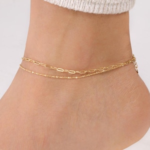 May include: A gold chain anklet with two different chain styles. The anklet is on a person's ankle.